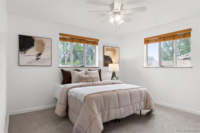 Staged bedroom with neutral bedding, two windows with wood blinds, and a ceiling fan.