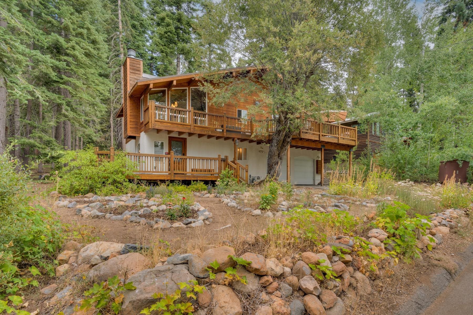 Wood-sided home with wraparound decks nestled among trees, with a rock garden in front.