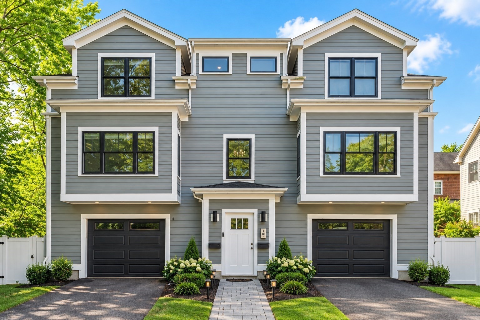 Gray two-story duplex with white trim, two black garage doors, and a landscaped central entrance.