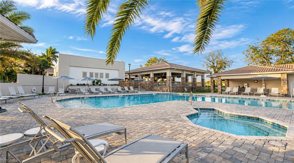 Community pool and spa with a paved deck, lounge chairs, and palm trees.