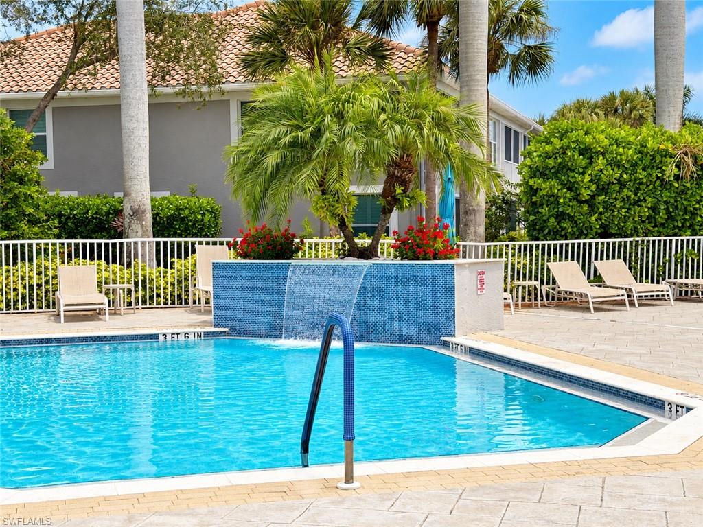 Outdoor swimming pool with a blue tile waterfall, palm landscaping, and lounge chairs.