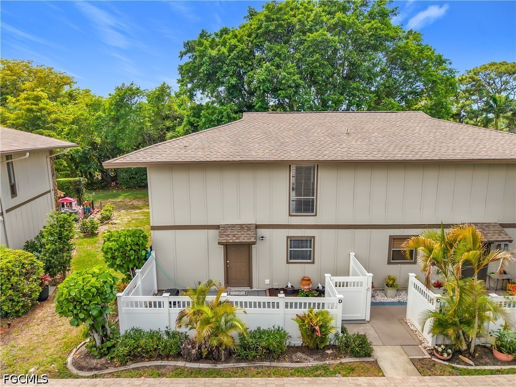 Two-story beige townhouse with white-fenced patios and landscaped gardens, viewed from above.