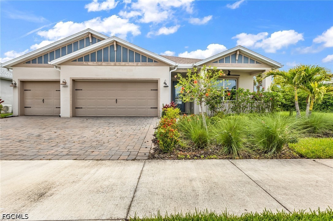 Single-story stucco home with a two-car garage, paver driveway, and tropical landscaping.