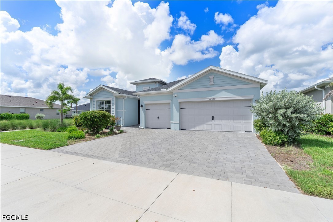 Light blue home with two white garage doors, a wide paver driveway, and landscaped lawn.