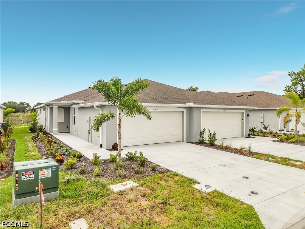 Gray attached home with two white garage doors, a wide driveway, and palm landscaping.