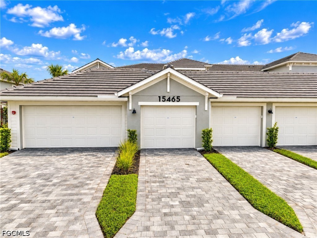 Front exterior with gray stucco, tiled roof, multiple garage doors, and paved driveways.