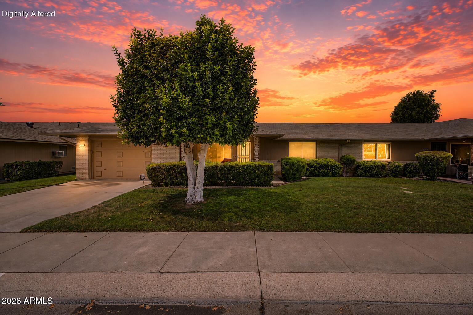 Single-story ranch home with brick facade and mature trees beneath a vivid sunset sky.