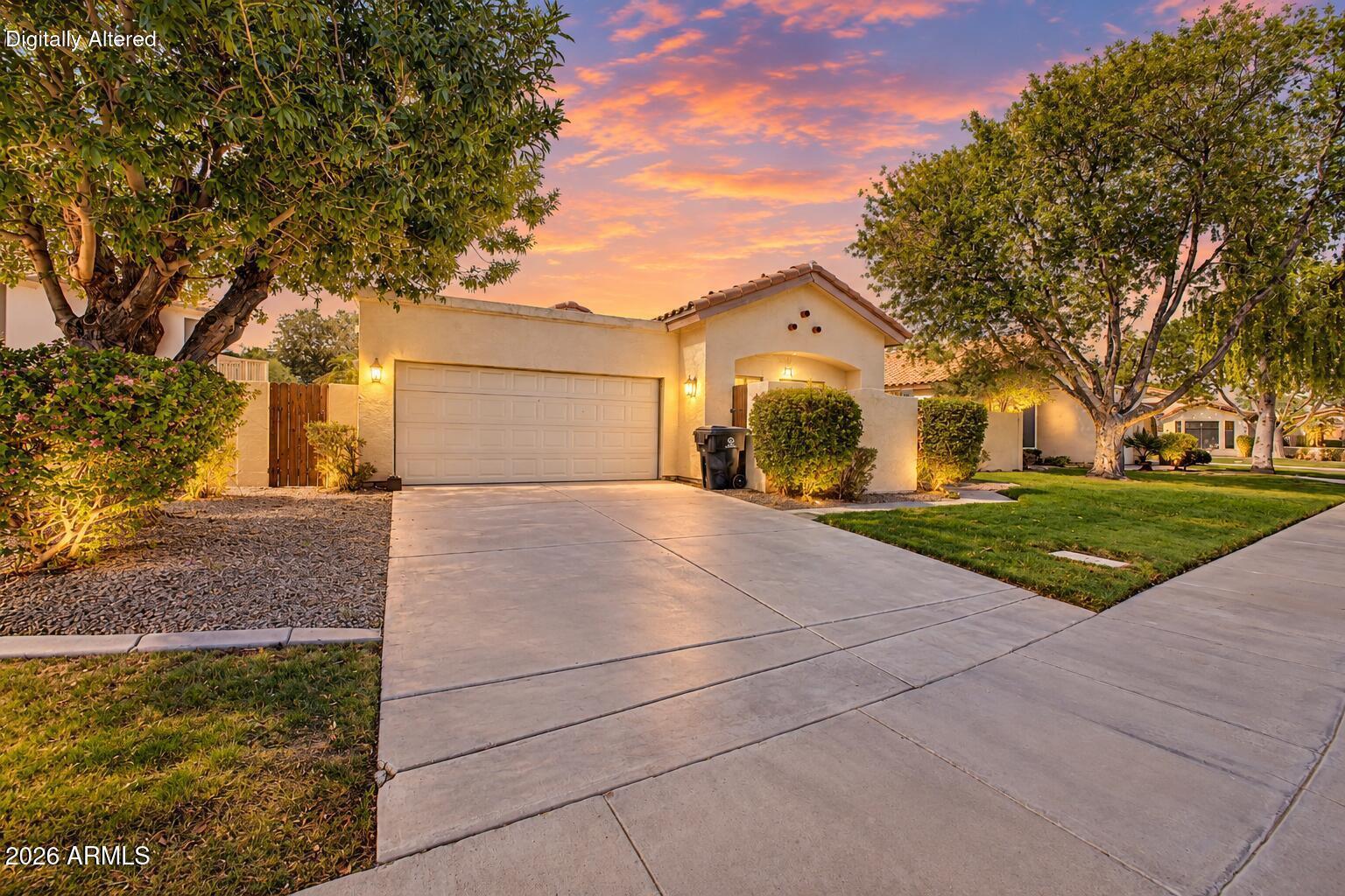 Stucco home with a two-car garage, broad driveway, and mature trees at sunset.