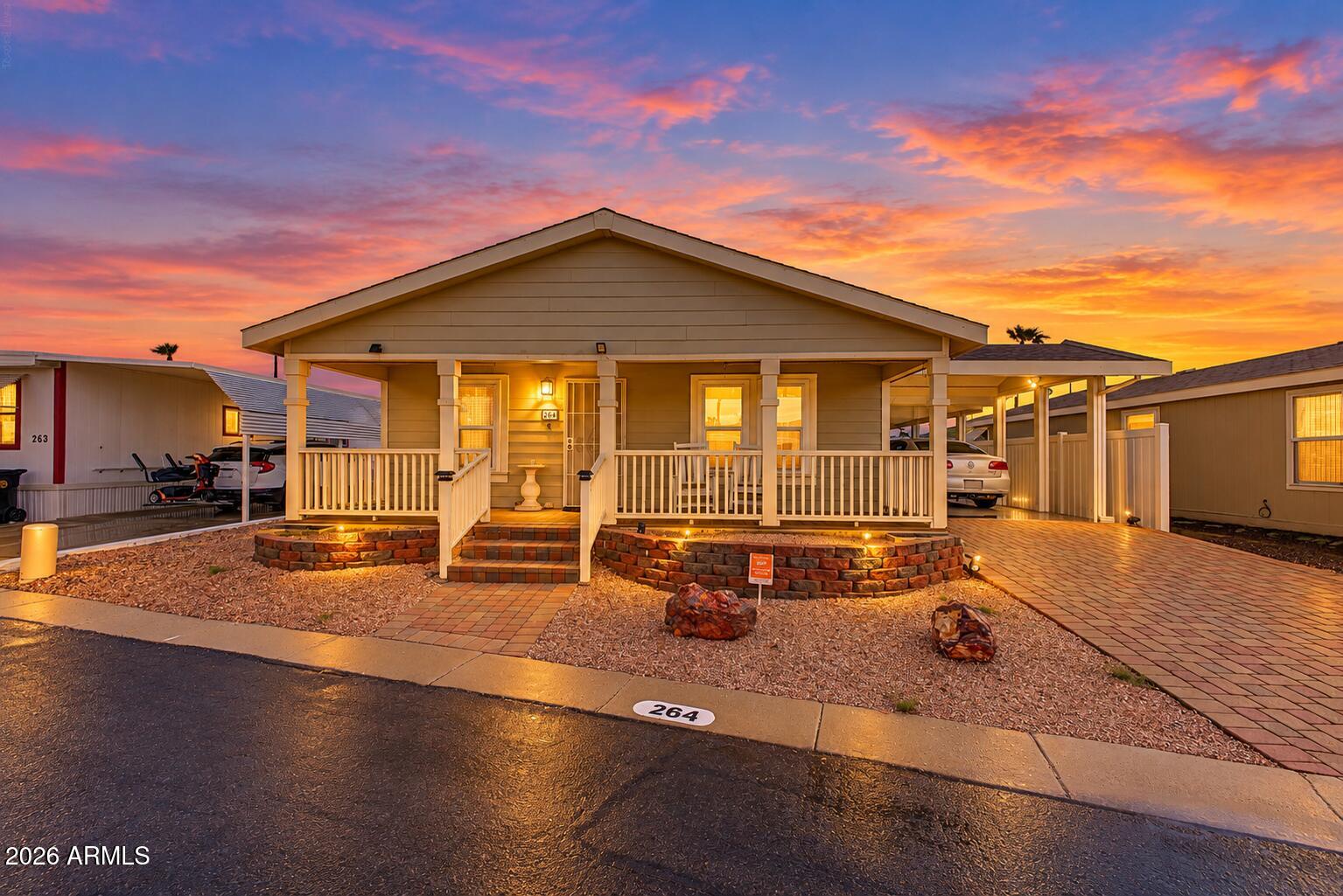 Manufactured home with a covered porch and carport beneath a vivid sunset.