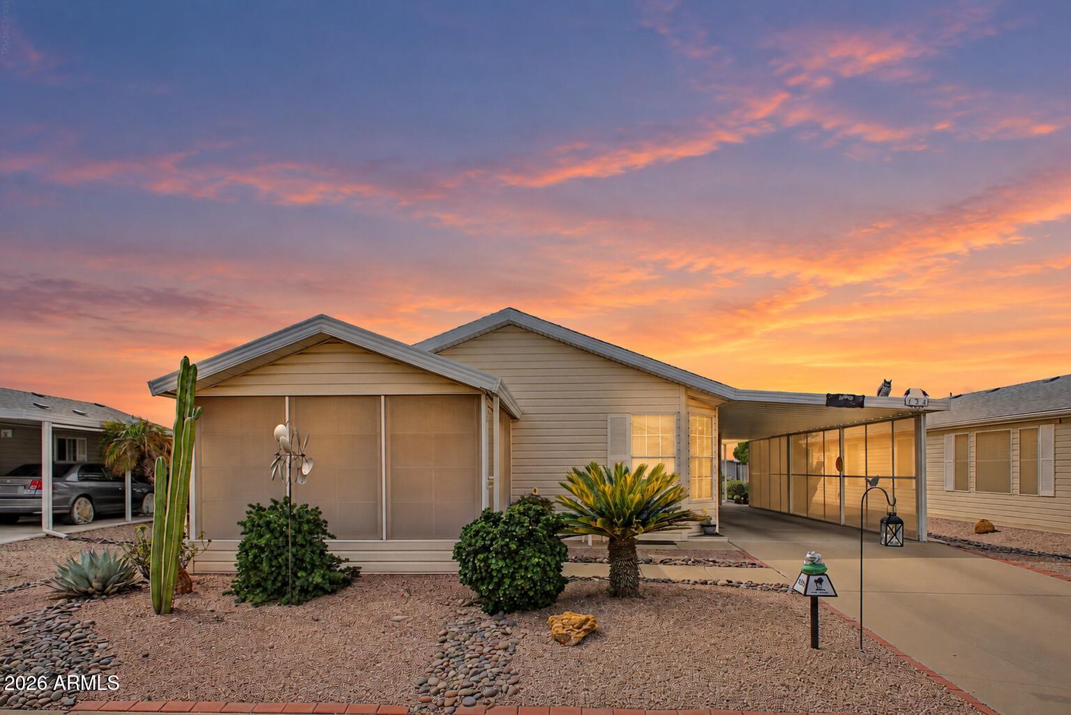 Single-story beige home with a screened patio and desert landscaping beneath a colorful dusk sky.