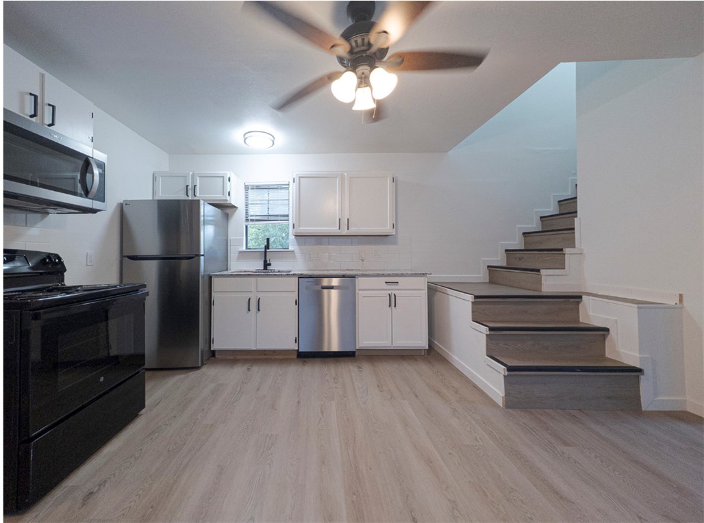 Vacant kitchen with stainless steel appliances and a staircase beside the cabinets.