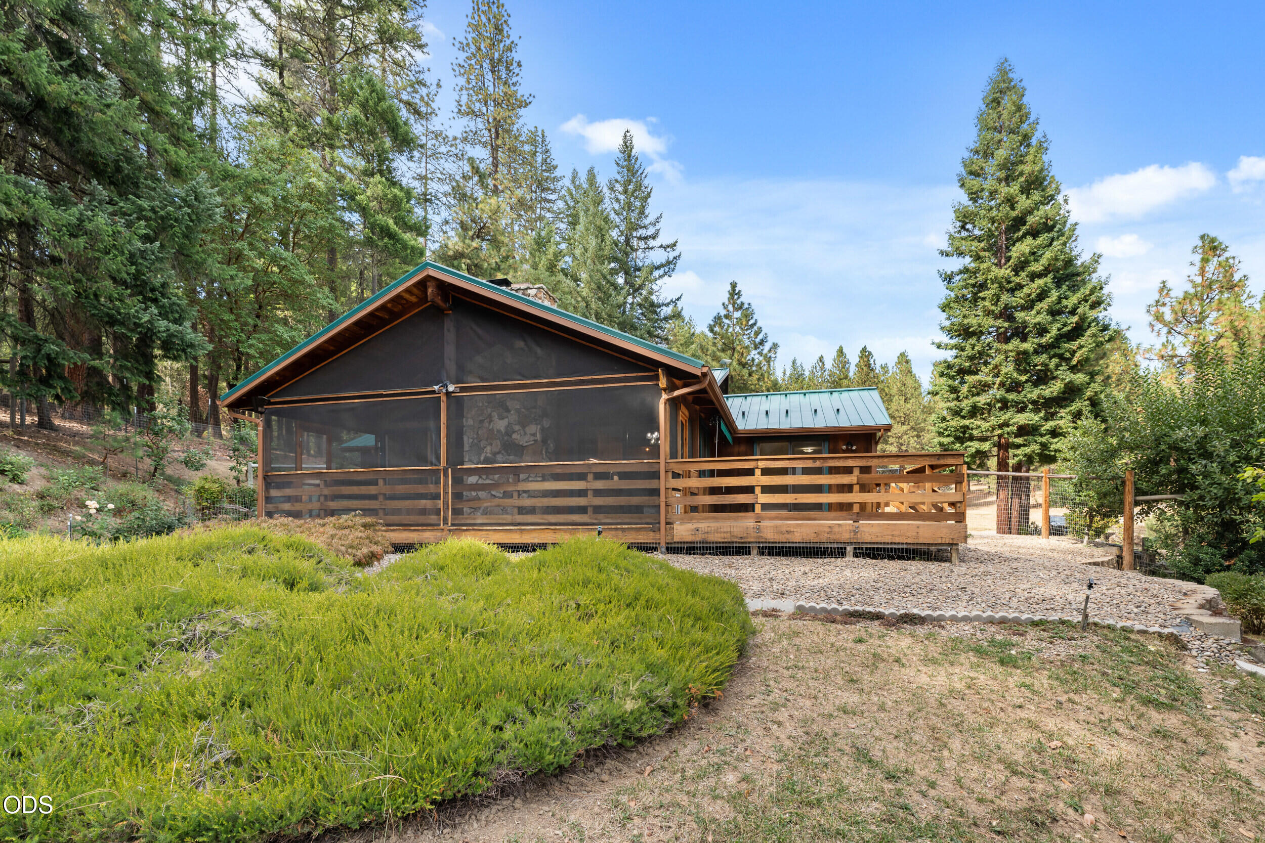 Rustic home with a screened porch and wooden deck among tall trees.