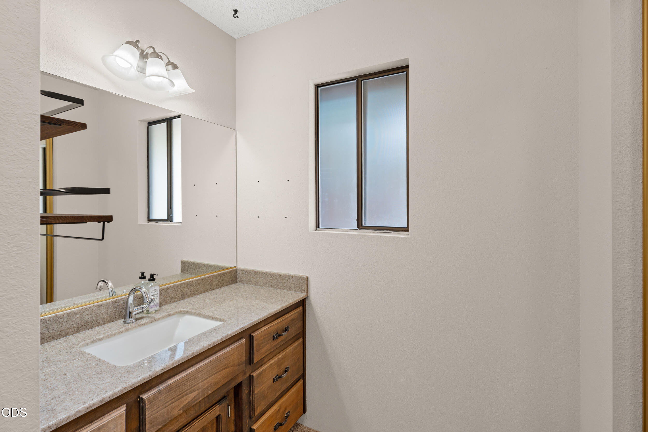 Bathroom vanity with wood cabinetry, a stone countertop, and frosted-glass windows.