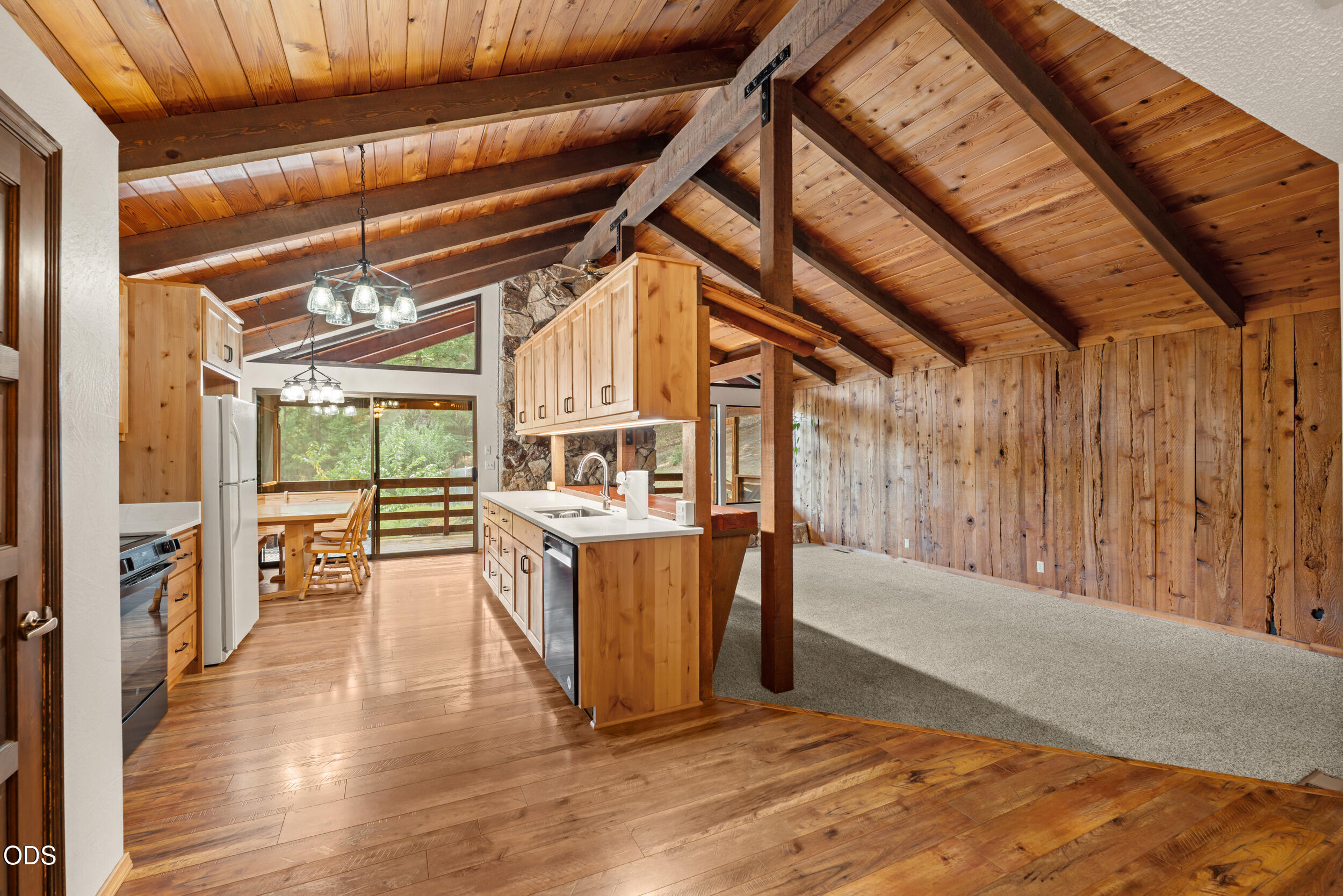 Open kitchen and living area with vaulted wood ceilings, exposed beams, and a stone accent wall.