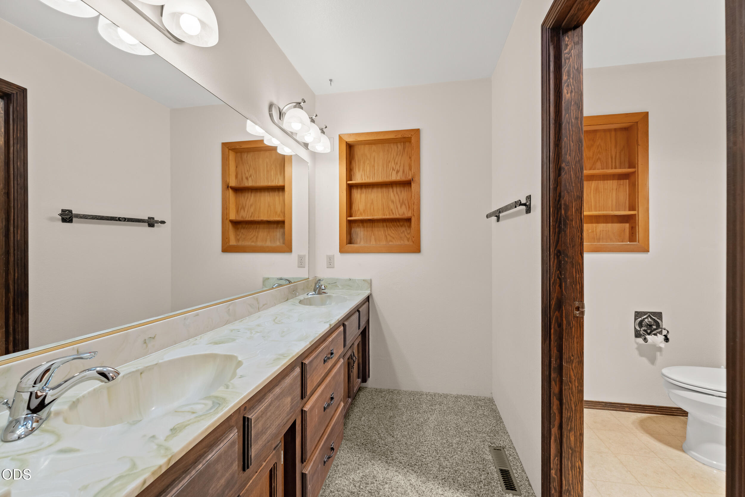 Bathroom with a double-sink vanity, marble-pattern counter, dark wood cabinets, and built-in shelves.