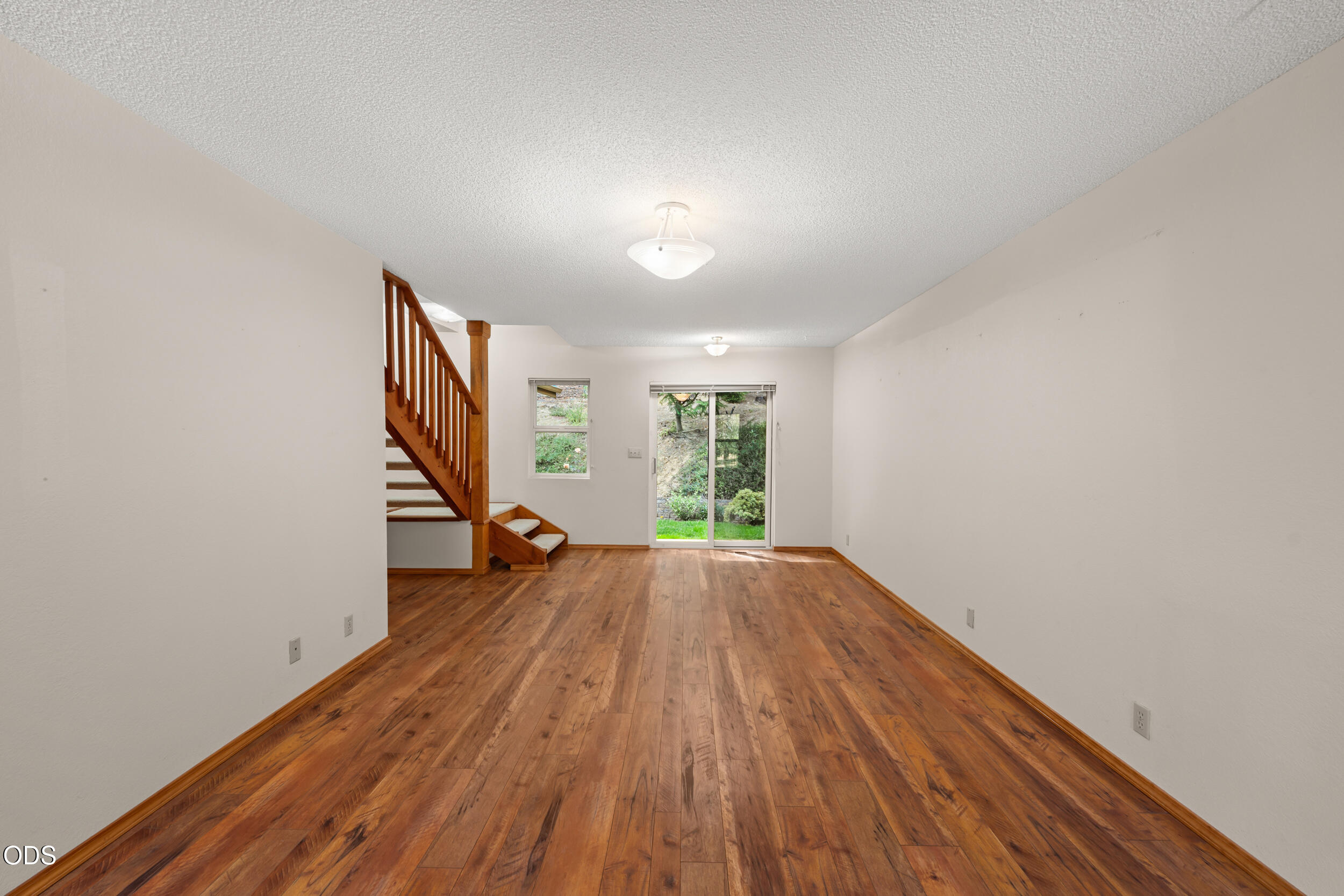 Vacant living room with hardwood floors, a wooden staircase, and a sliding glass door to the yard.