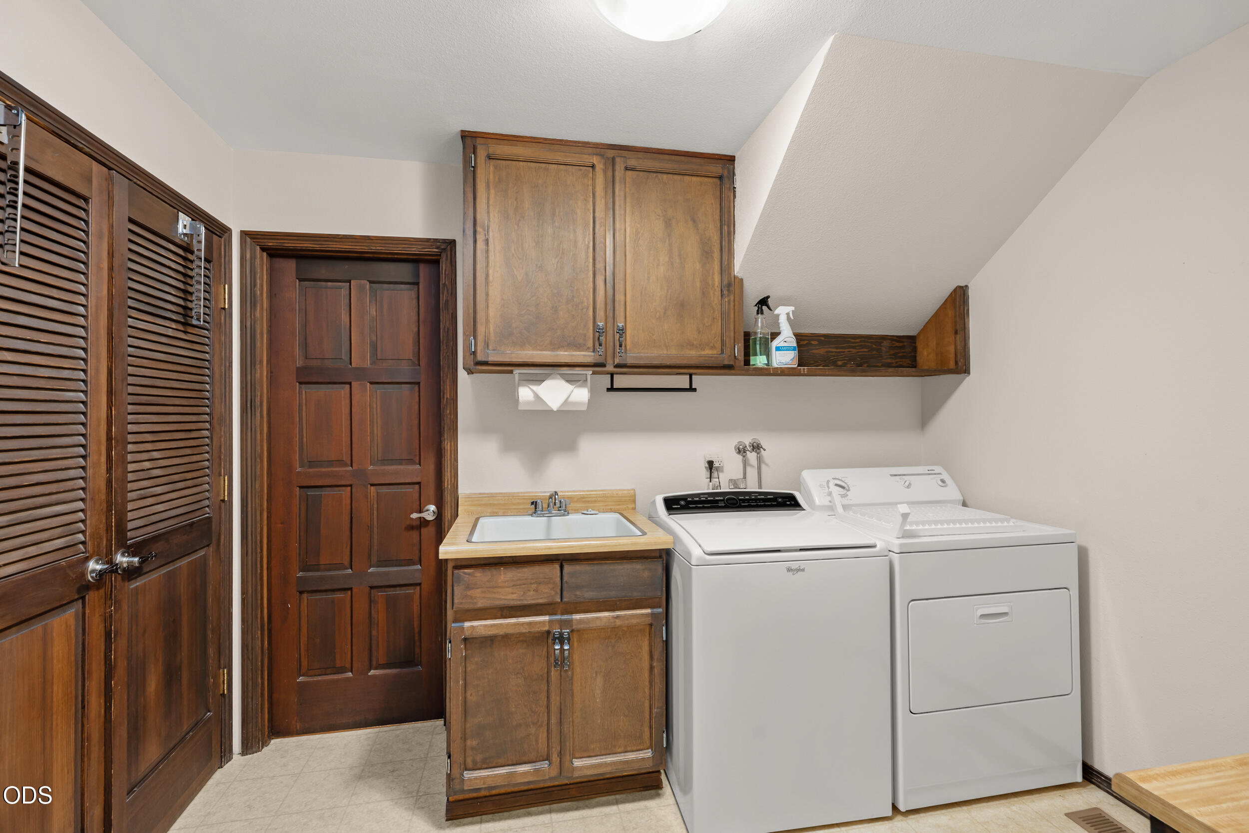 Laundry room with washer and dryer beside a utility sink and dark wood cabinetry.