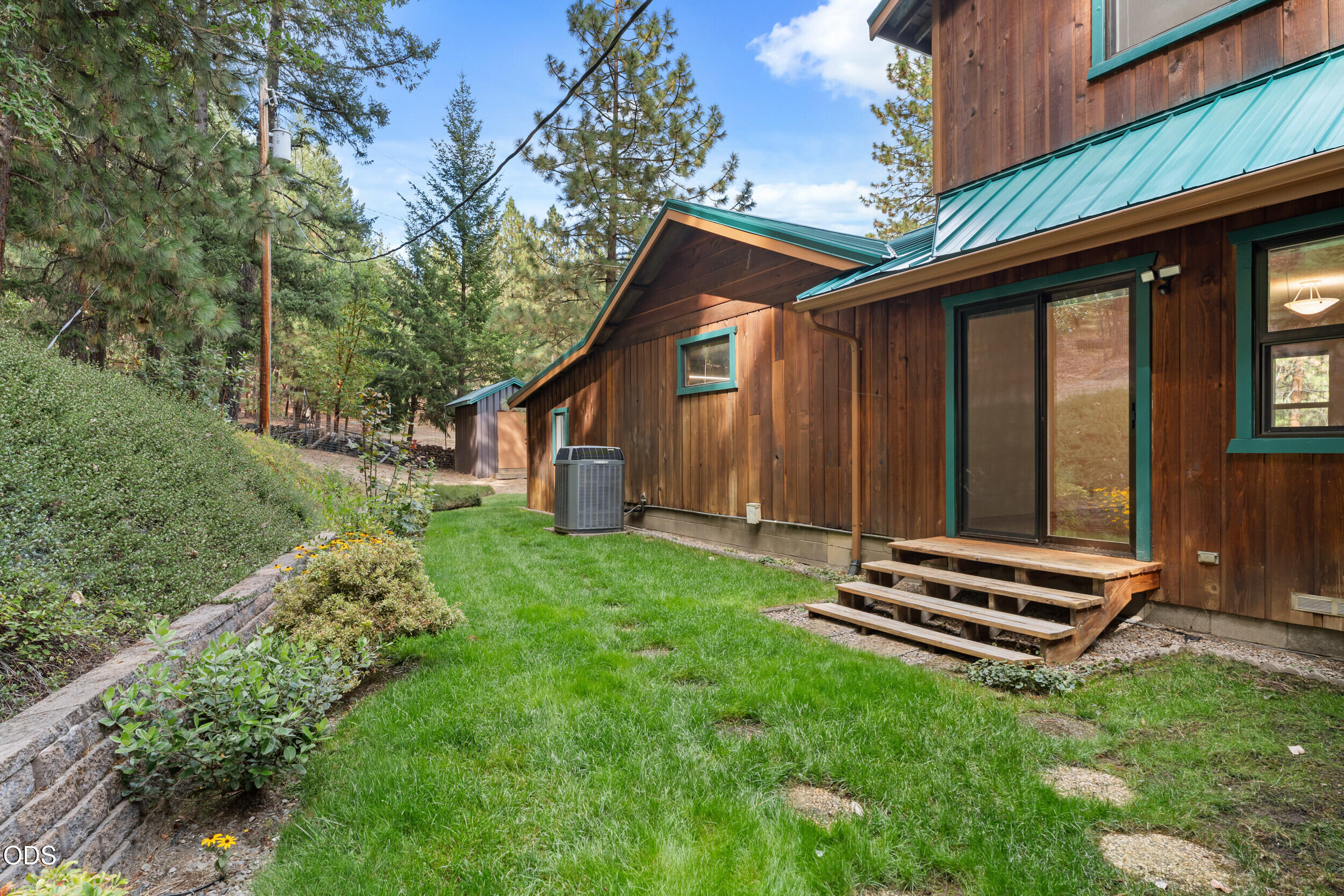 Wood-sided home with teal metal roof beside a grassy yard and tall trees.