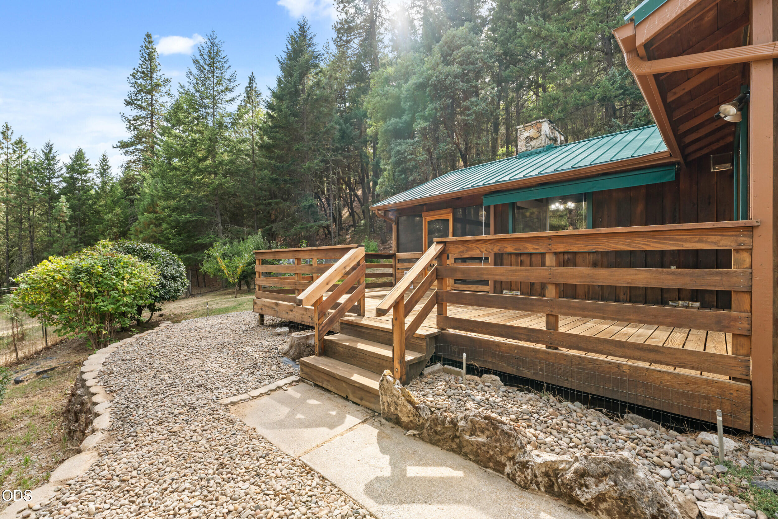 Wood-sided home with a raised wooden deck, green metal roof, and wooded surroundings.