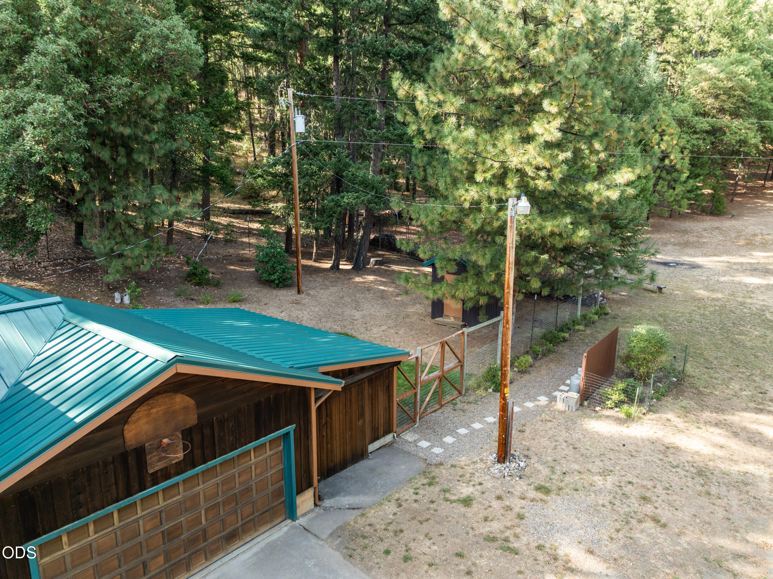 Elevated view of a teal-roofed garage beside a fenced, tree-lined yard.