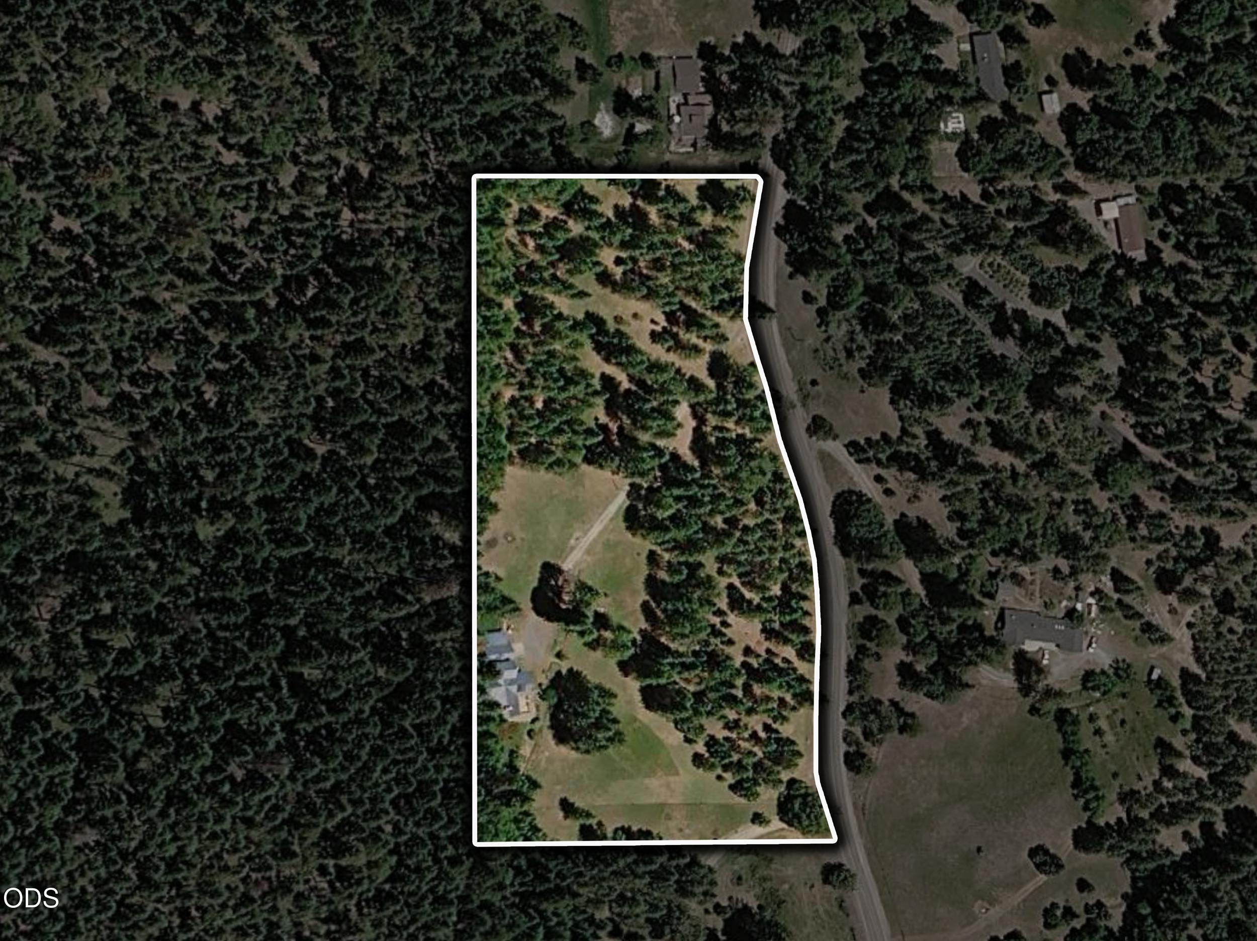 Aerial view of a wooded parcel outlined in white, with a house, clearings, and a road along one side.