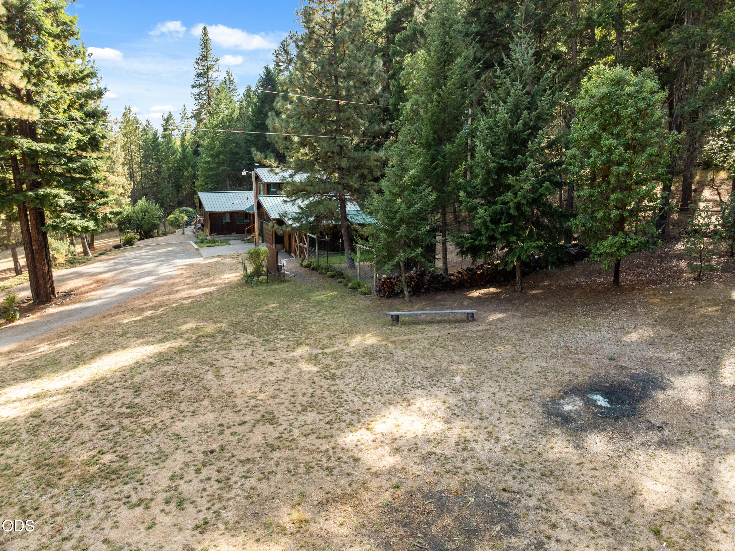Wooded cabin with metal roofs, a broad dry-grass yard, and gravel driveway.