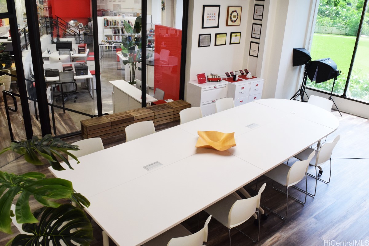 Office conference room with a long white table, glass partitions, and windows overlooking a lawn.