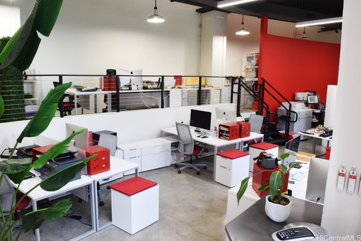 Open-plan office with a mezzanine, white desks, black railings, and a bright red accent wall.