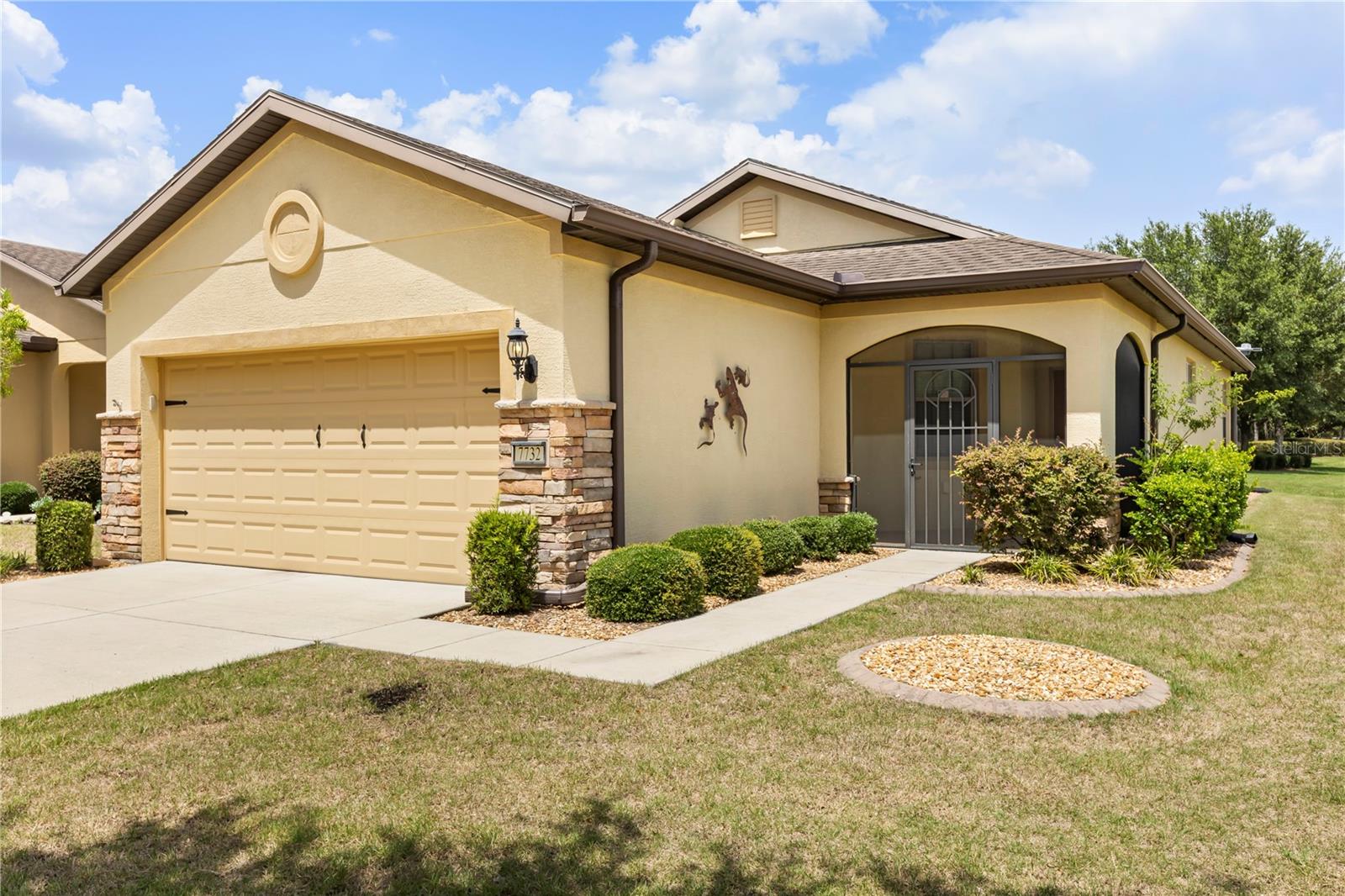 Beige stucco home with a two-car garage, stone accents, and a covered front entry.