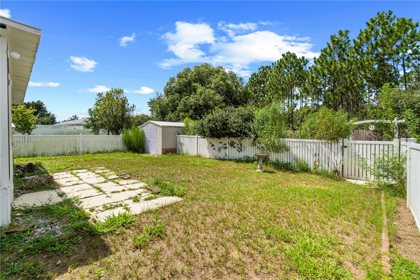 Fenced backyard with a stepping-stone path, small shed, and mature trees.