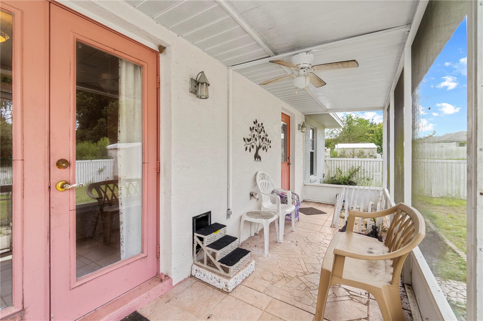 Covered patio with pink-framed glass doors, tiled flooring, a ceiling fan, and outdoor seating.
