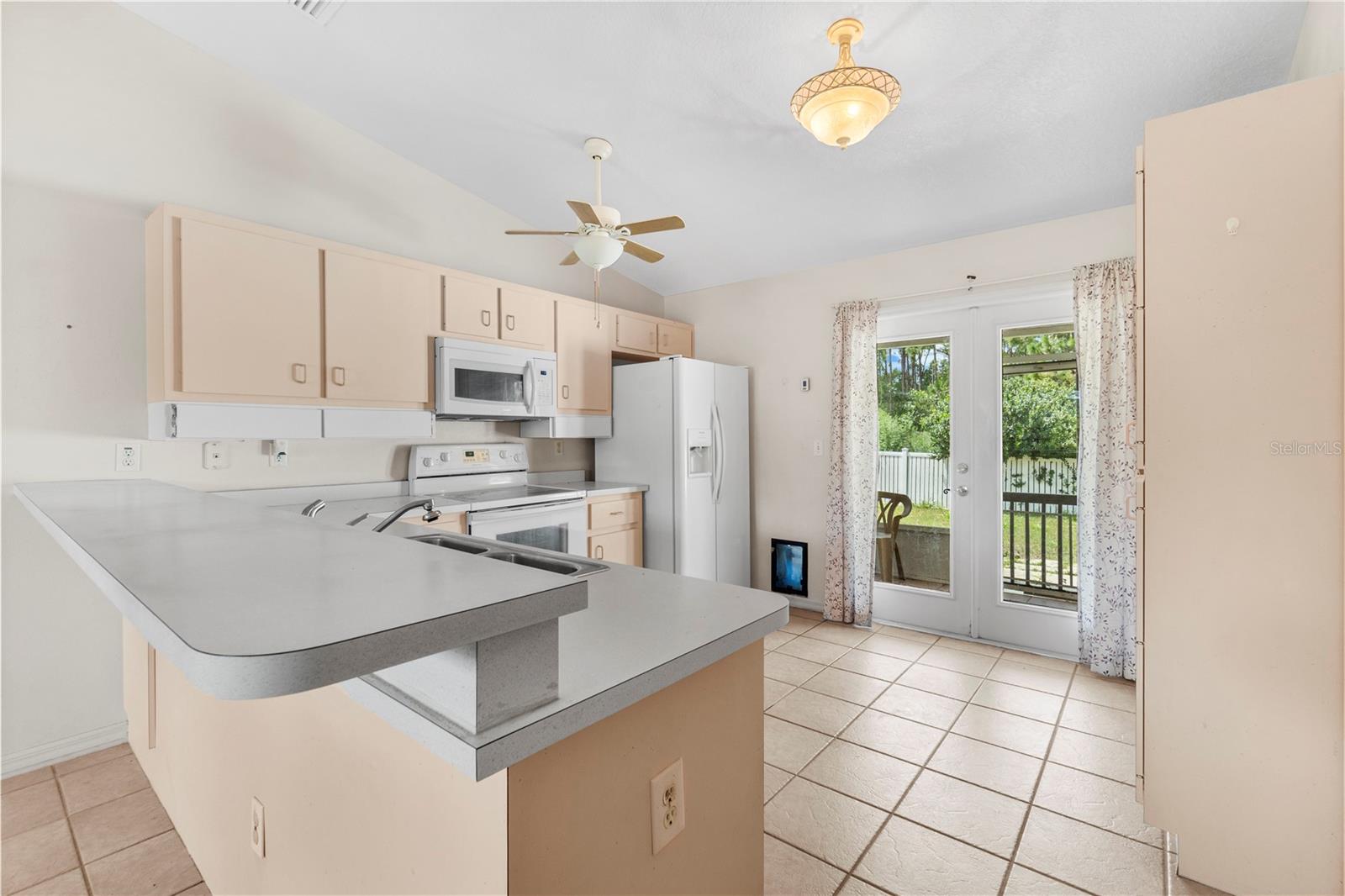 Kitchen with a large peninsula, white appliances, and glass doors opening to a patio.