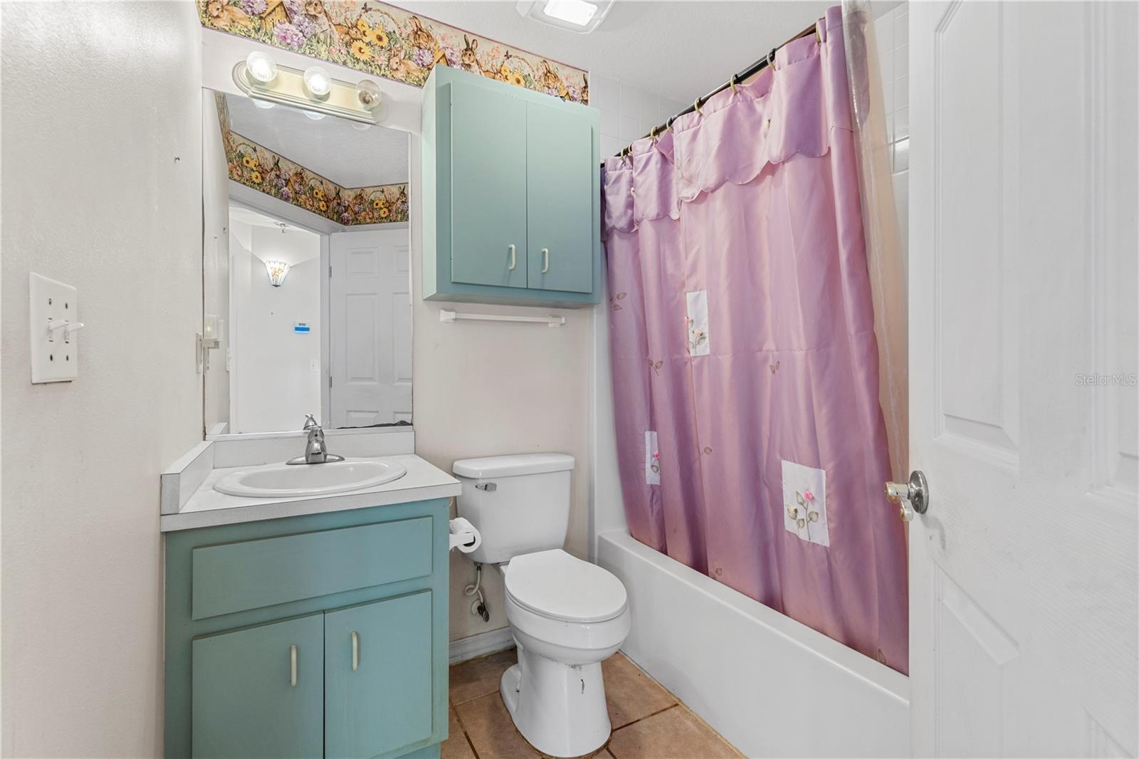 Bathroom with turquoise vanity, white fixtures, and a pink floral shower curtain.