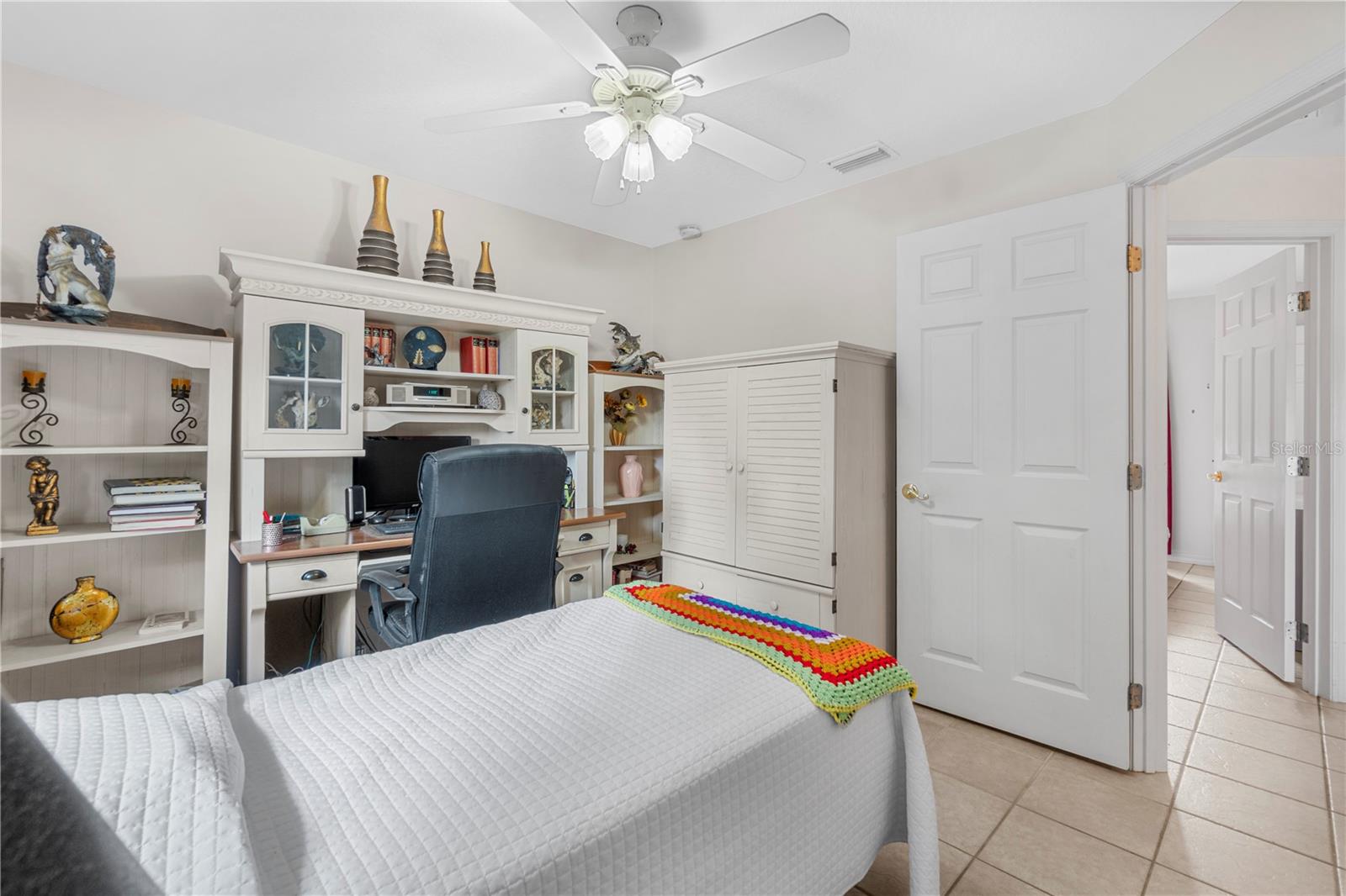 Bedroom with a white bed, colorful crocheted throw, and built-in desk and shelving.