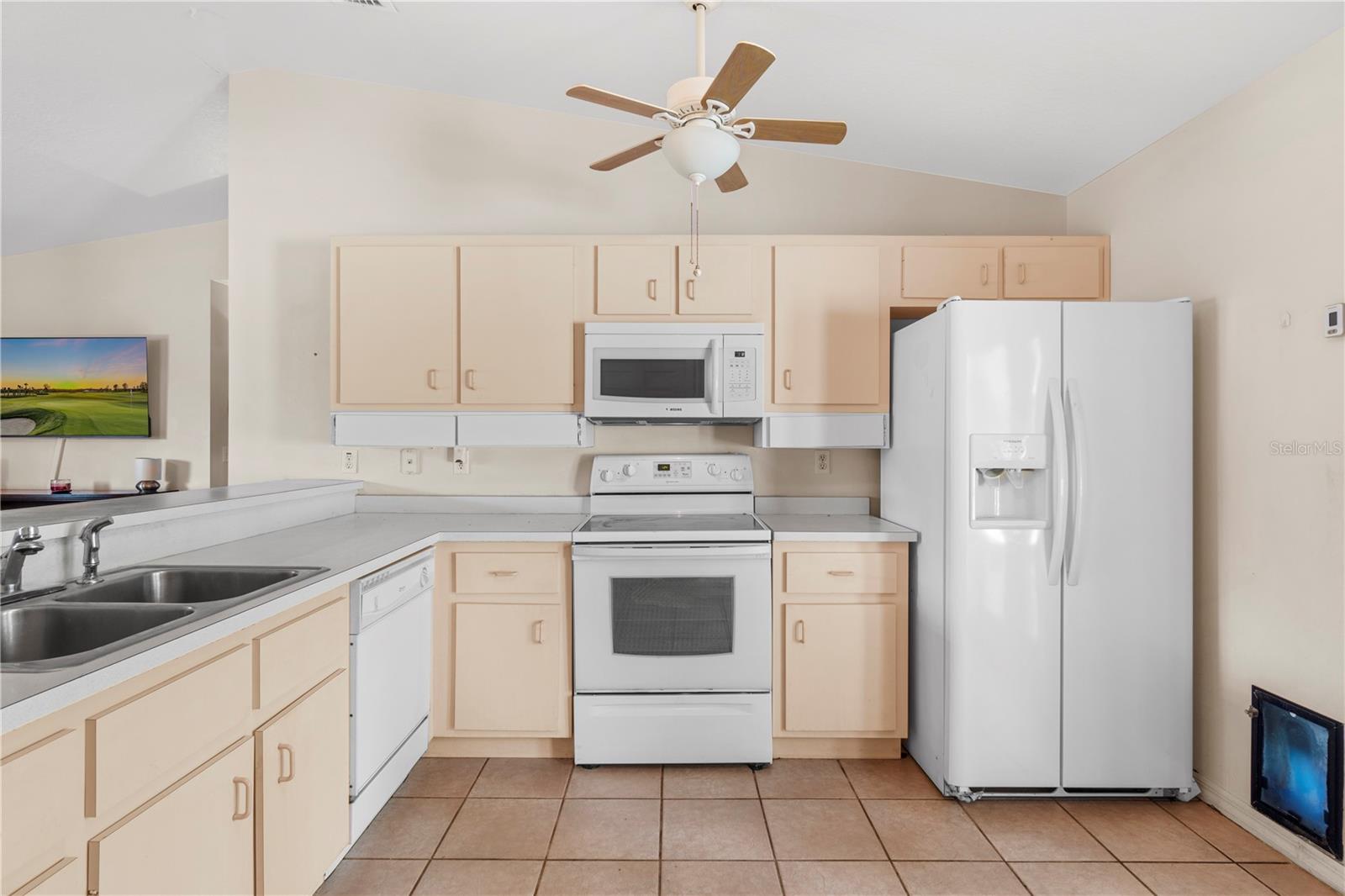 Kitchen with light wood cabinets, white appliances, and a double-basin sink.
