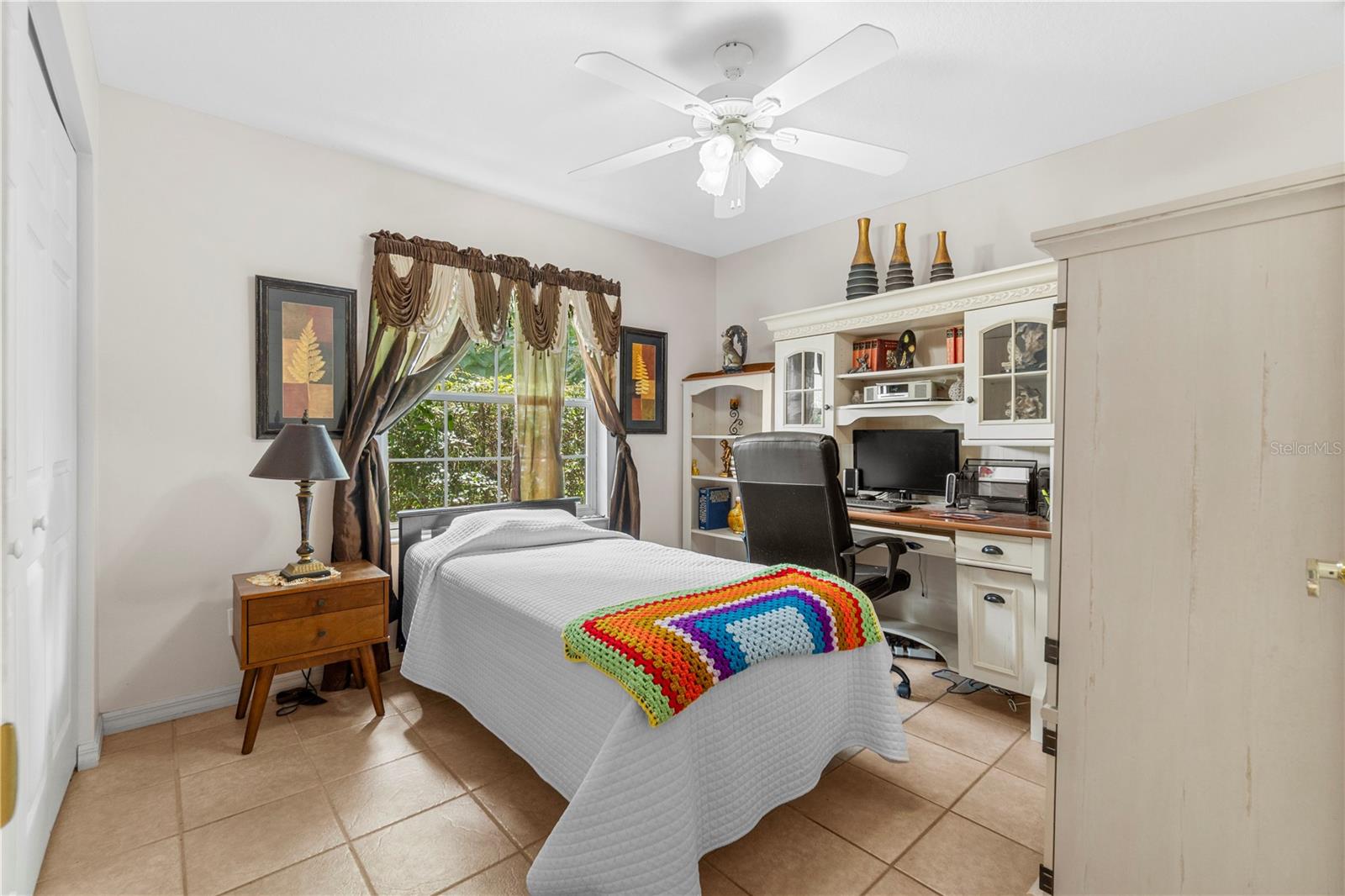 Bedroom with a colorful crocheted blanket and built-in desk beneath shelving.