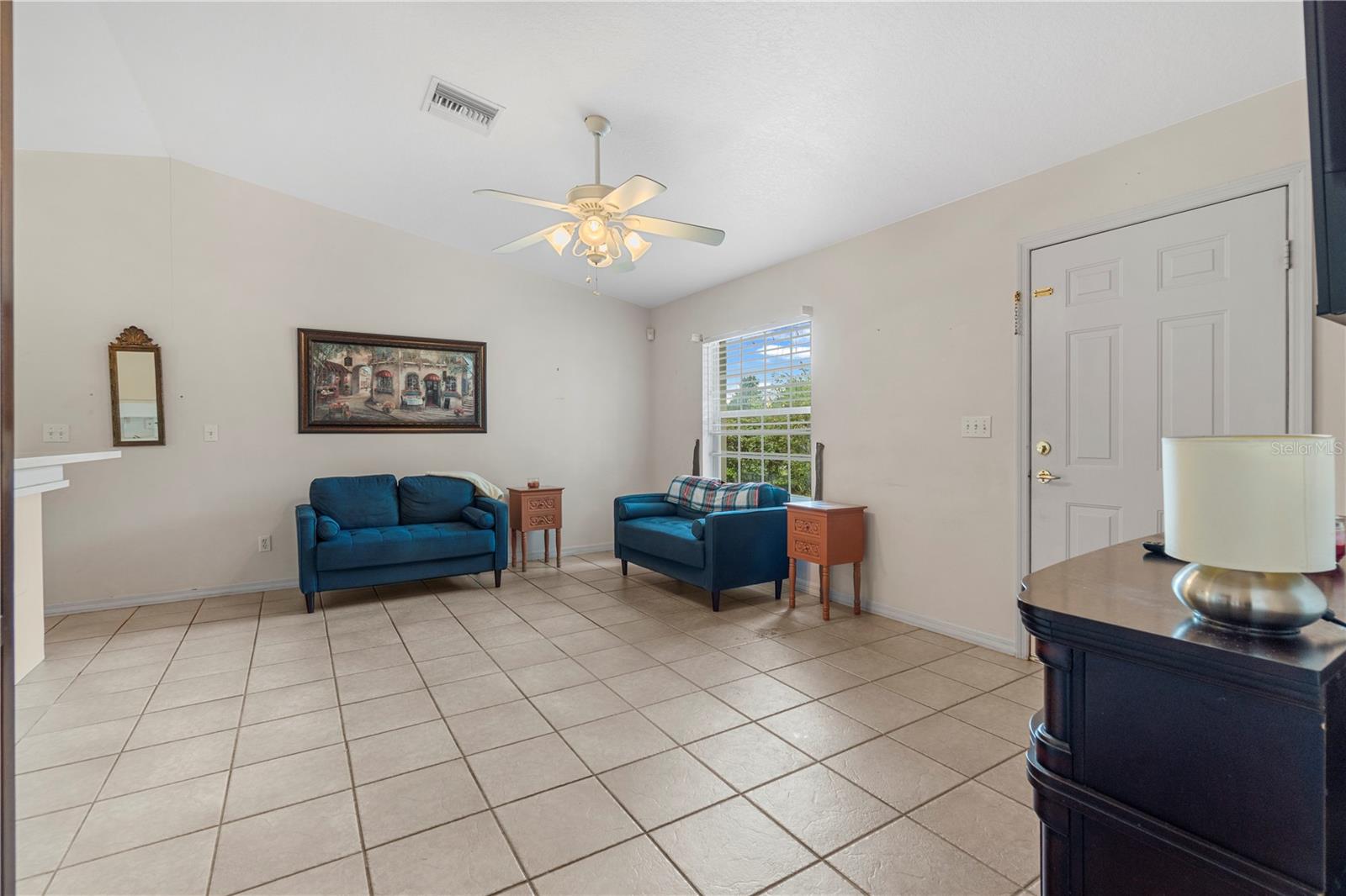 Living room with two blue sofas, tiled floors, and a ceiling fan.