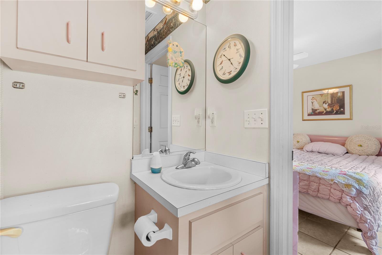 Bathroom vanity and toilet, with a pink bedroom visible through the doorway.
