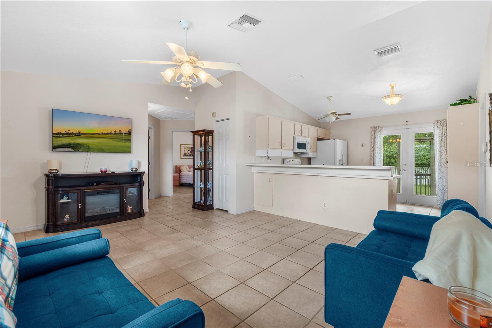 Open-plan living room and kitchen with blue sofas, tiled floors, and a breakfast bar.