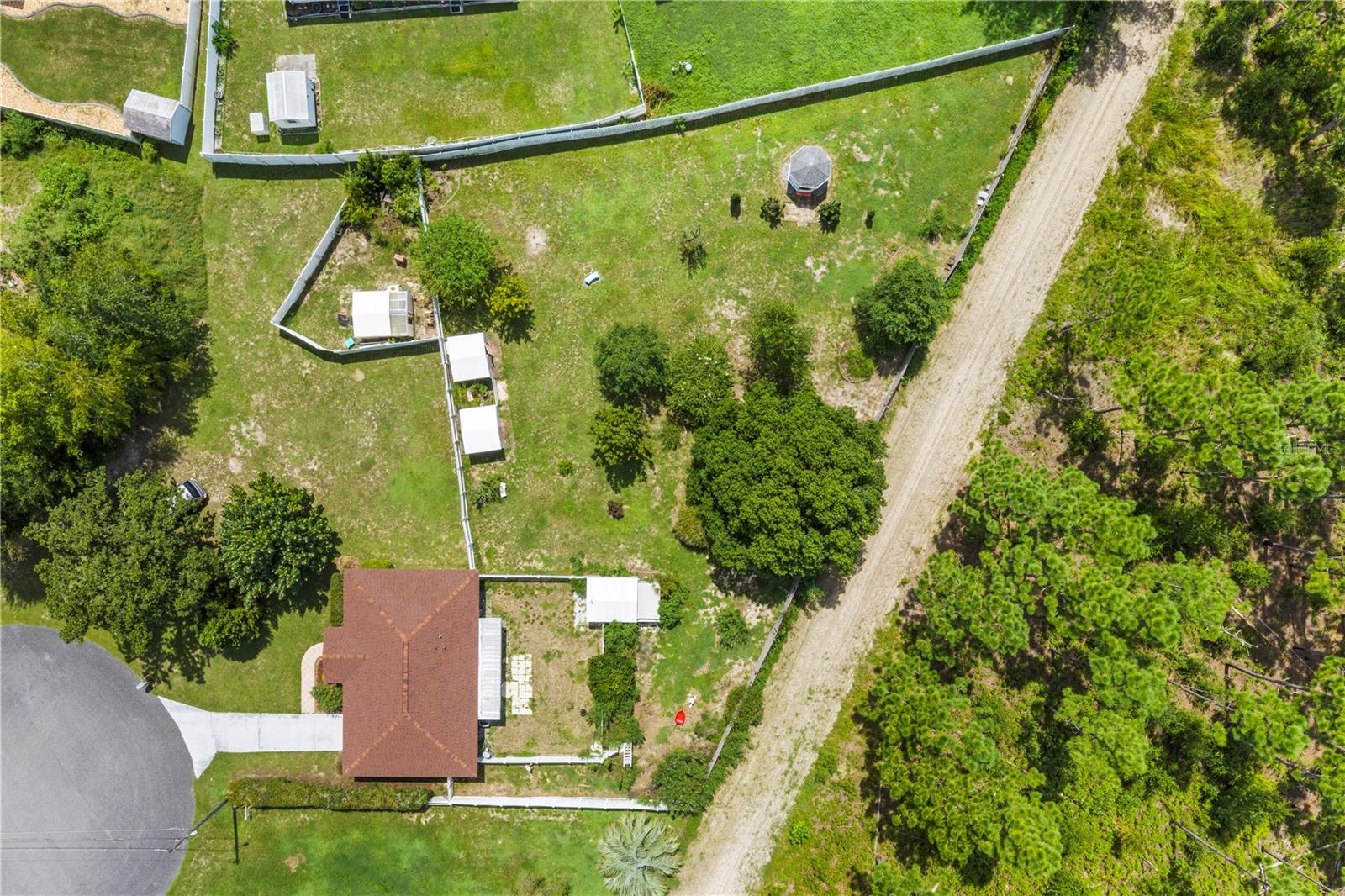 Aerial view of a fenced property with a single-story house, grassy yard, and dirt road.