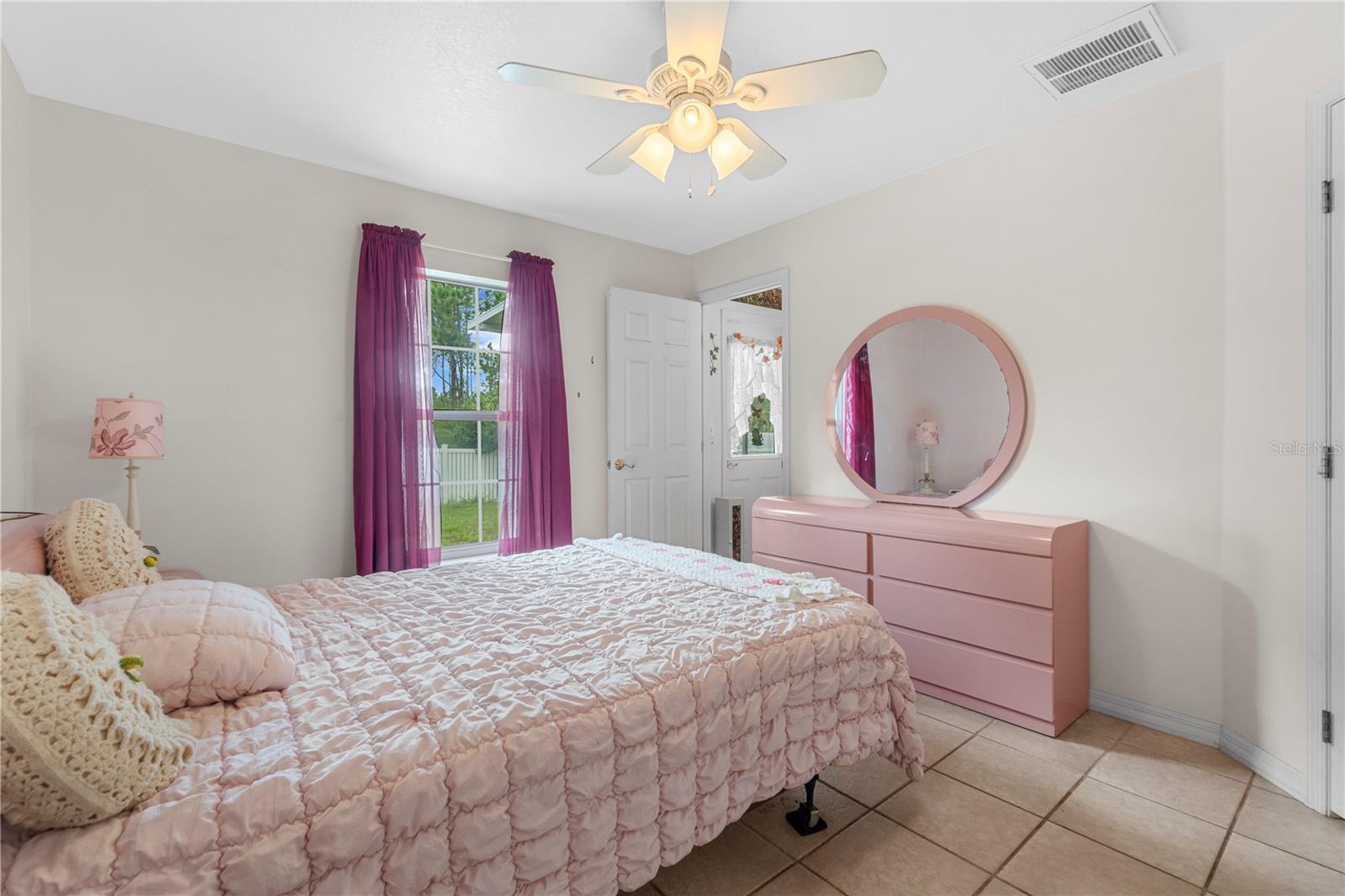 Bedroom with a pink quilted bed, matching dresser, and purple curtains.