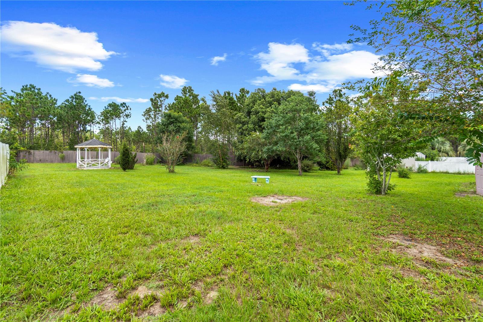 Fenced grassy backyard with mature trees and a white gazebo.