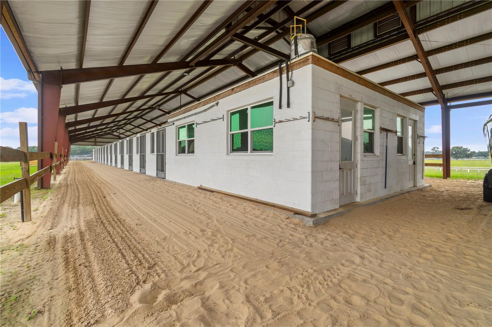 Covered stable with white block stall rooms and a wide sandy aisle.