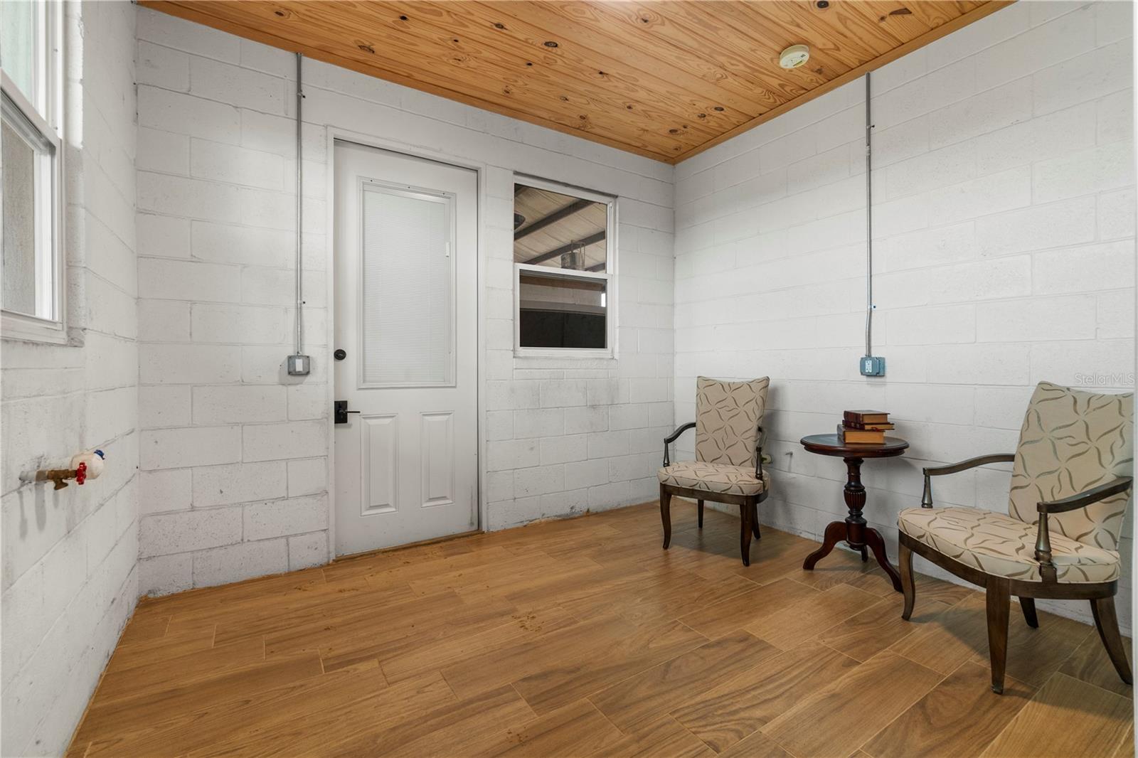 Enclosed sitting room with a wood ceiling and floor, white block walls, and two armchairs.