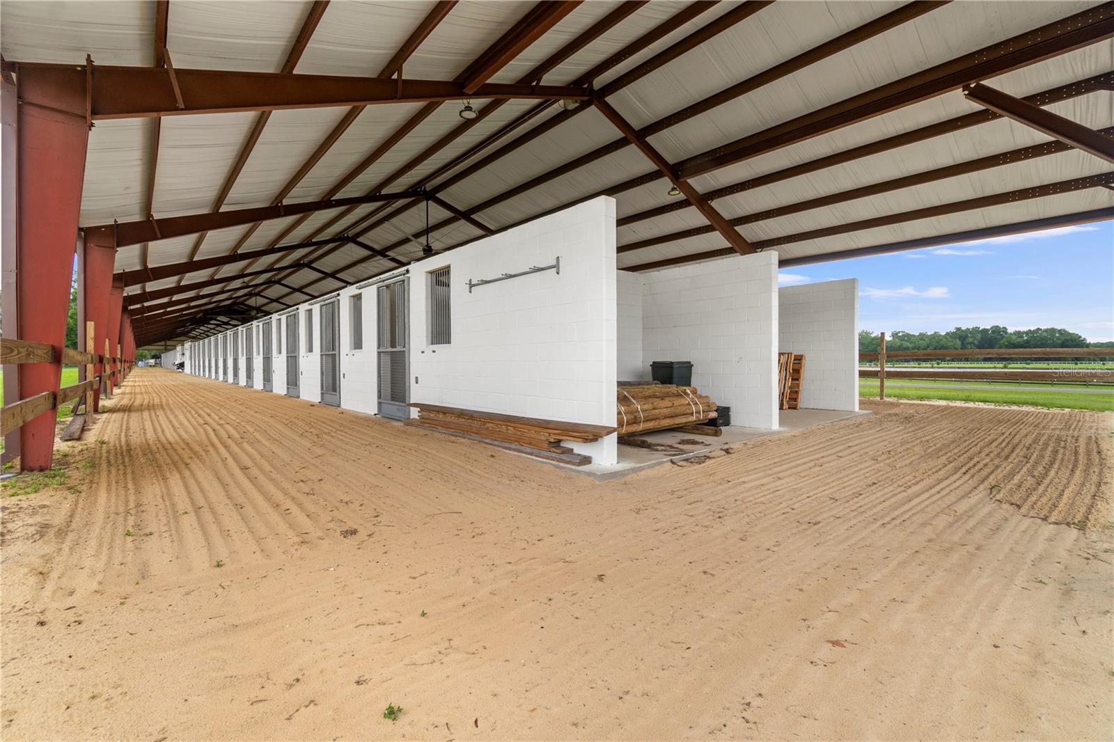 Covered stable with a long row of white stalls and a broad sandy area.