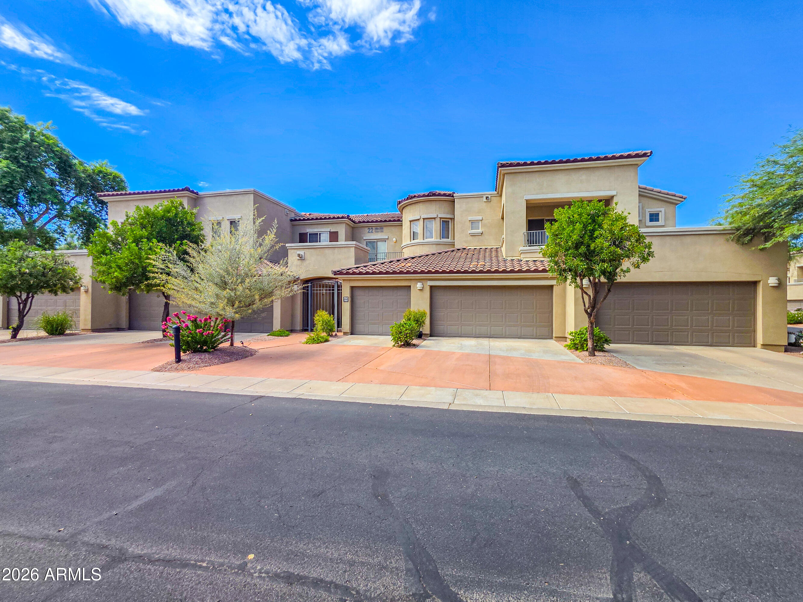 Tan attached homes with red tile roofs, multiple garages, and desert landscaping along the street.
