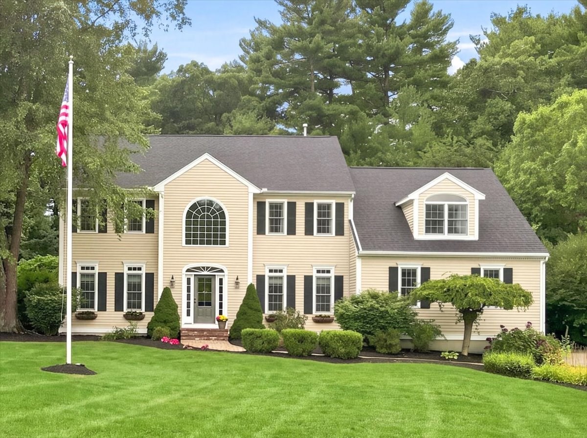 Pale yellow two-story home with an arched front window, landscaped lawn, and U.S. flag.