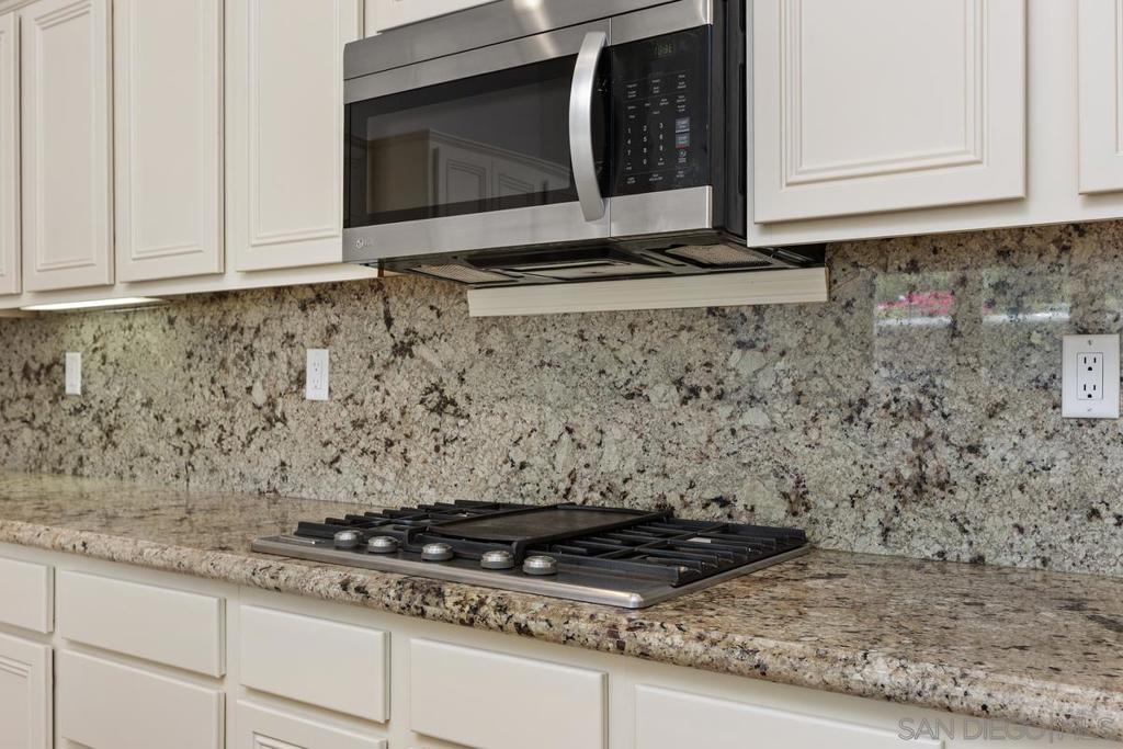 Kitchen with a gas cooktop, stainless steel microwave, and granite countertops and backsplash.