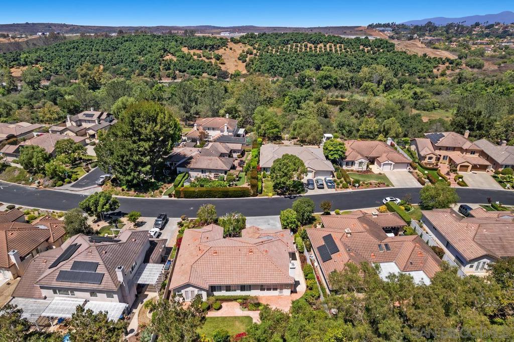 Aerial view of a tiled-roof home on a suburban street, with green hills and distant mountains behind it.