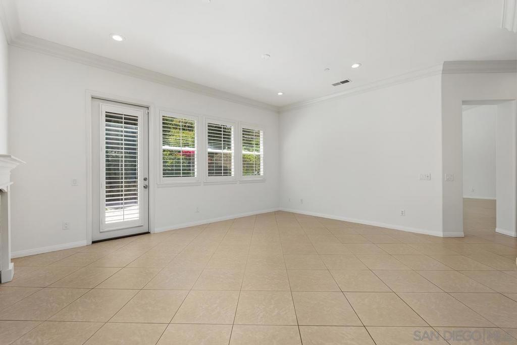 Vacant room with beige tile flooring, a glass patio door, and shuttered windows.